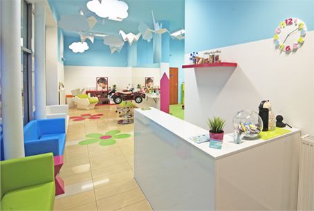 Biała recepcja i kolorowa poczekalnia, pod turkusowym sufitem wiszą origami-żurawie i chmurki