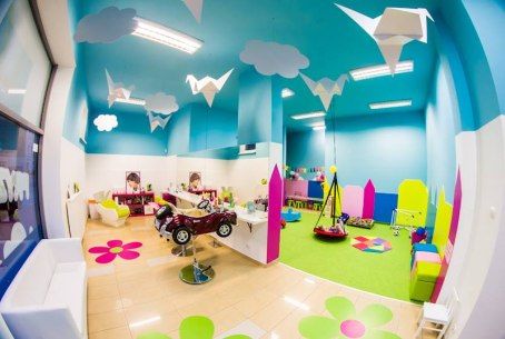 Wnętrze salonu Lolo Manolo: turkusowy sufit z chmurkami i origami, fotelik-autko i sala zabaw z huśtawką